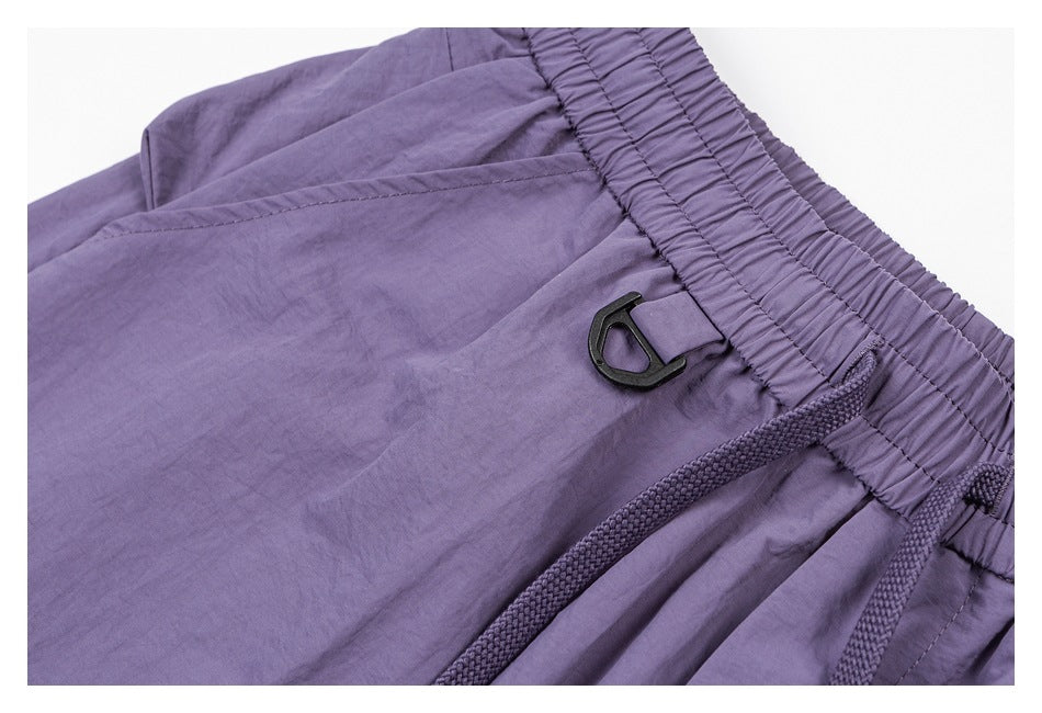 Close-up of purple pants showing the gathered elastic waistband, drawcord, and small black clip.