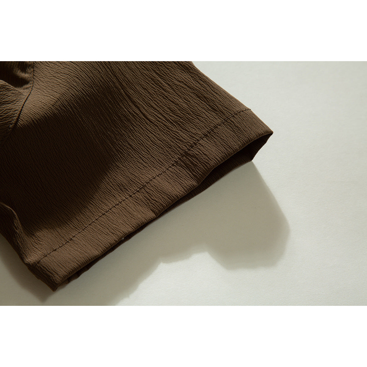 Close-up of the brown shirt's short sleeve and stitched hem.