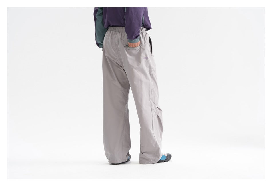 Rear view of a model wearing loose gray trousers with an elastic waist, back pocket, and blue-accented shoes.