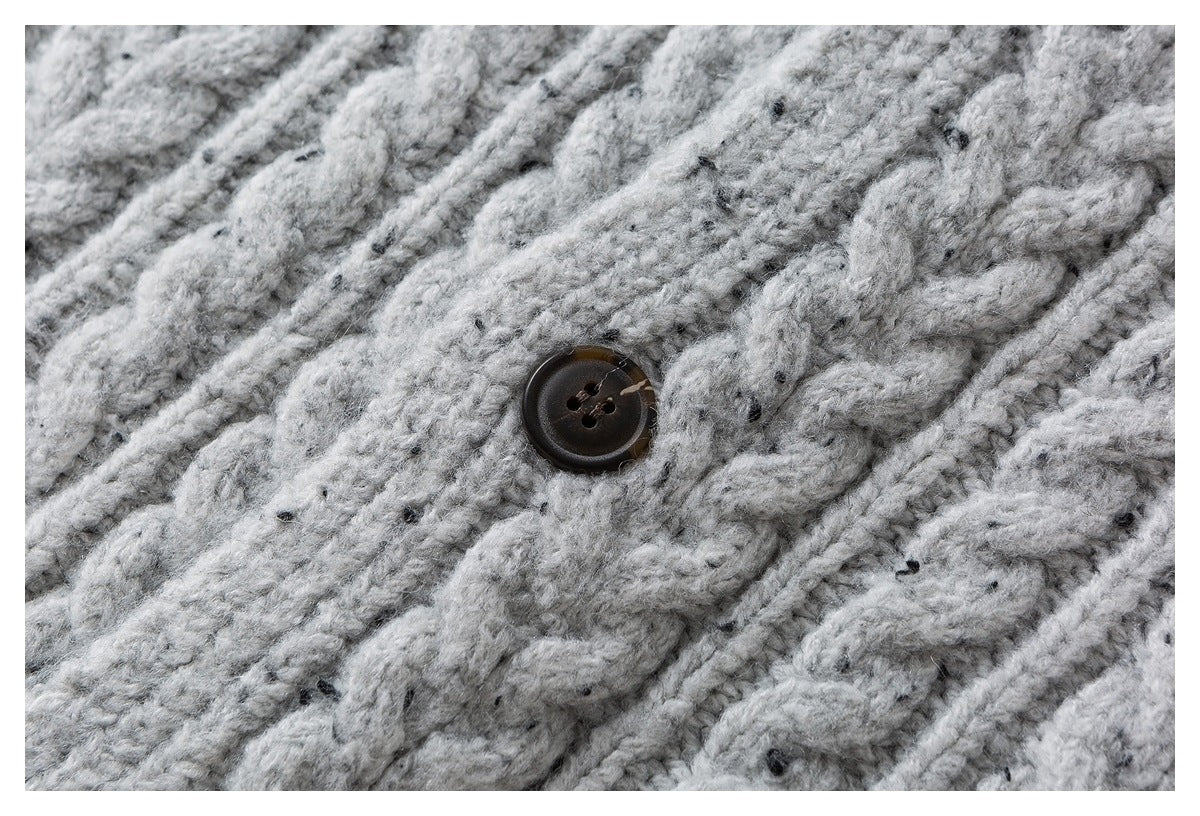Close-up of chunky light gray knit fabric with dark flecks and a dark four-hole button.