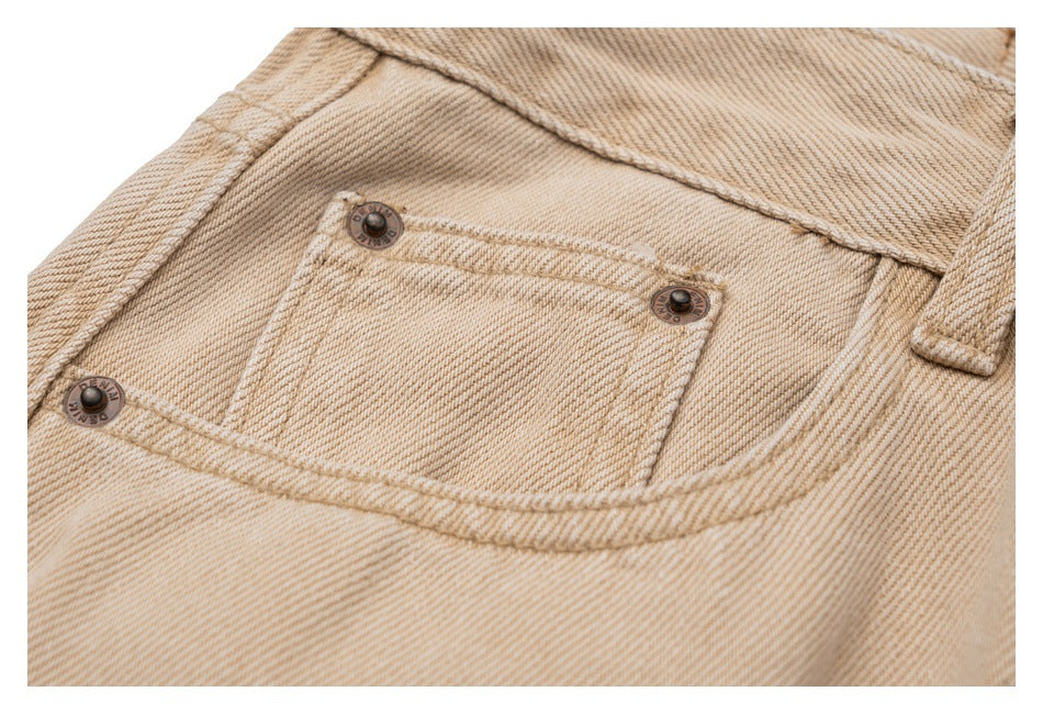 Close-up of beige twill trousers showing a small front pocket with metal rivets and double-stitched seams.