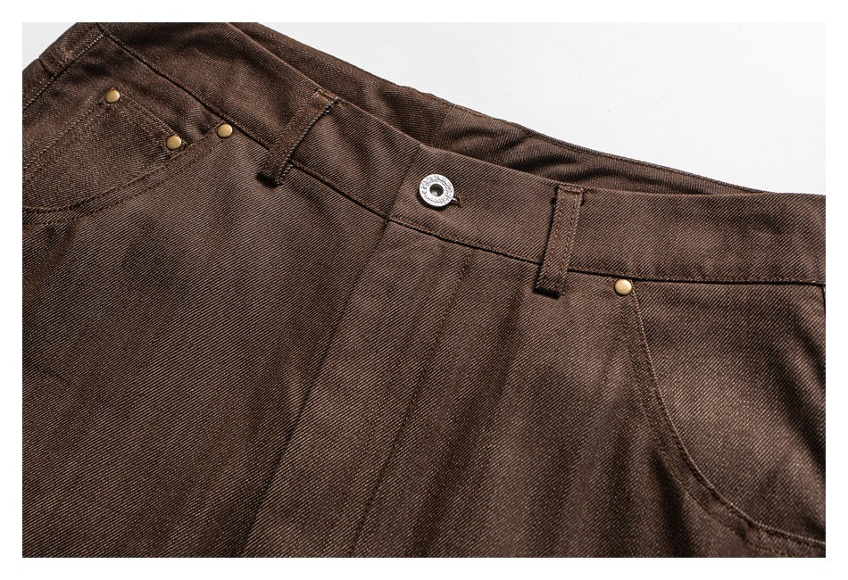 Close-up of brown trousers showing the waistband, belt loops, front pocket, metal button, and rivets.