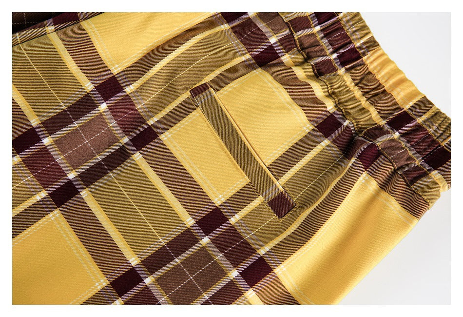 Close-up of mustard and brown plaid trousers showing a pocket and gathered elastic waistband.