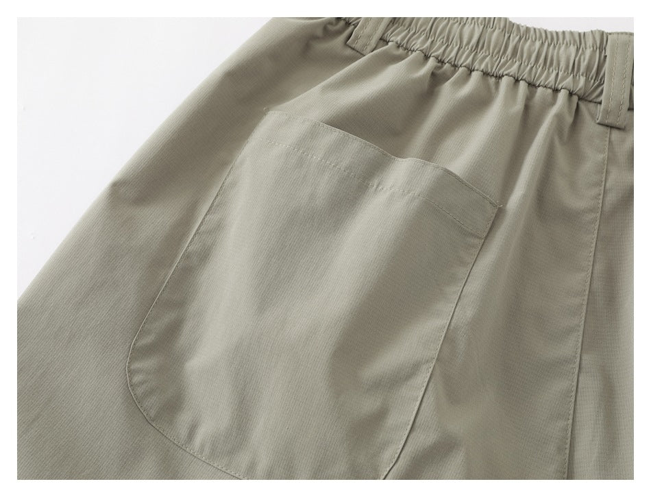Close-up of a large patch pocket and elastic waistband on light khaki shorts.