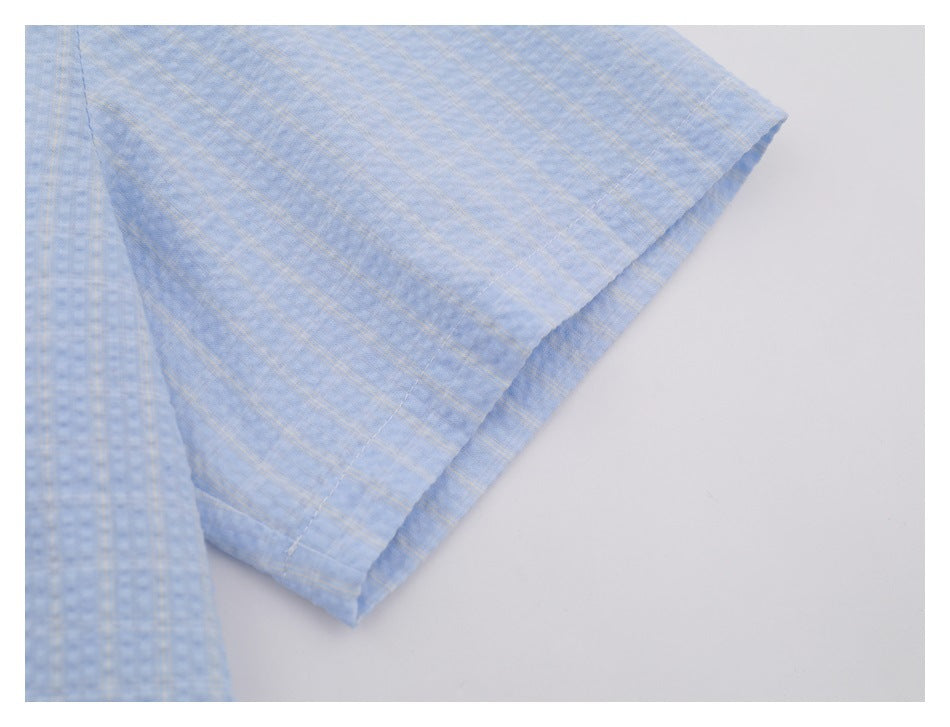 Close-up of the short sleeve and stitched hem of a light blue subtly checked shirt.