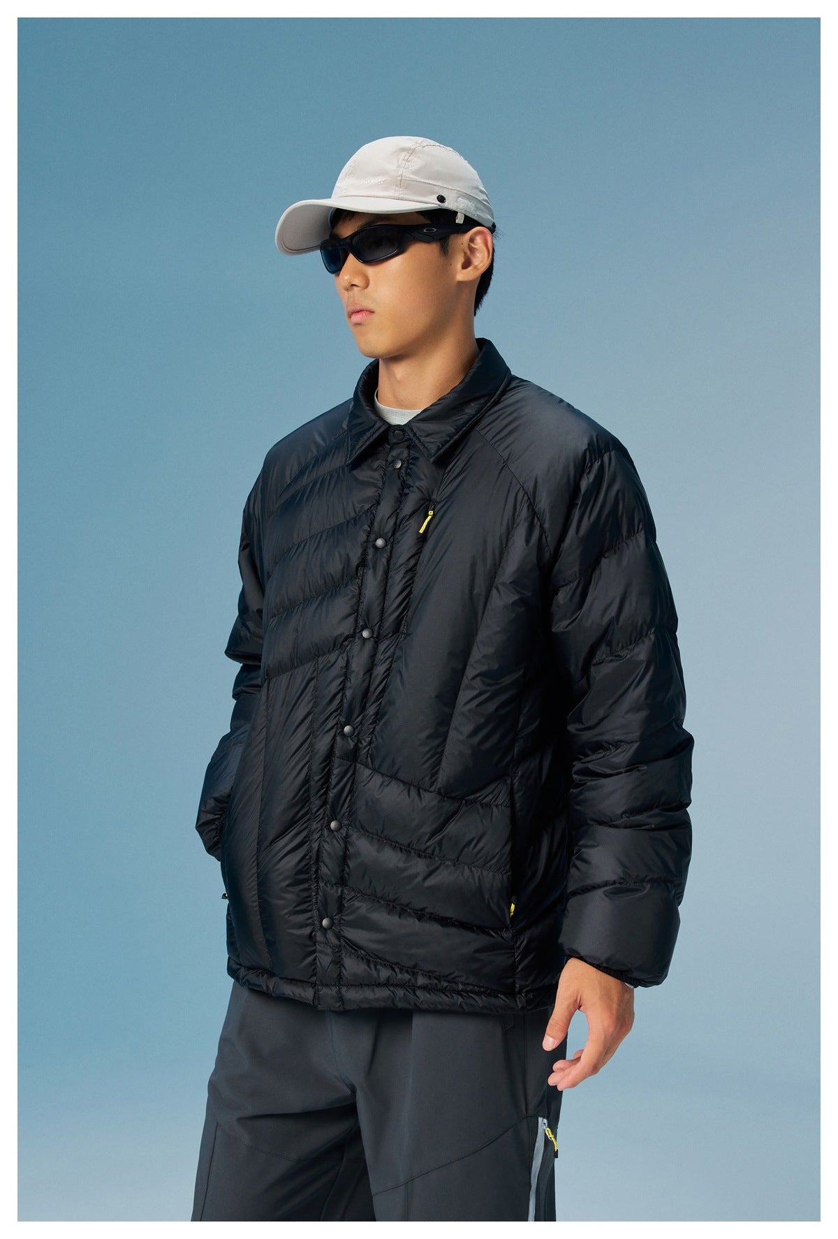 Angled view of a model wearing a black quilted snap-front jacket with a pointed collar and yellow zipper accents.