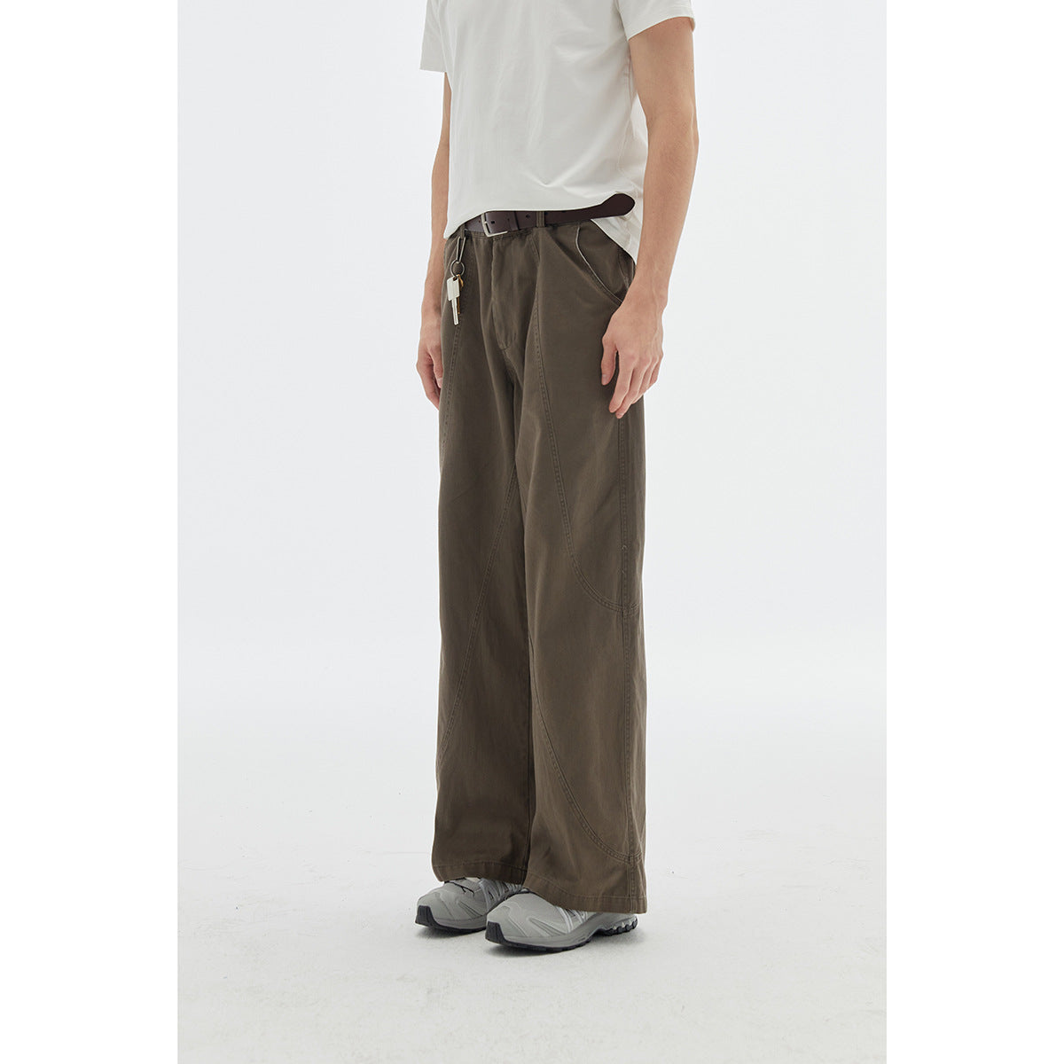 Cropped model view wearing wide-leg dark olive trousers with curved seam panels, a white T-shirt and gray sneakers.