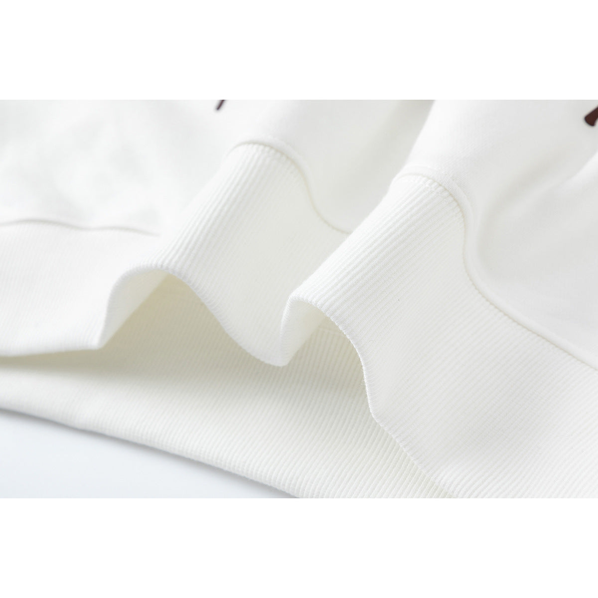 Close-up of white ribbed fabric gathered in soft folds, showing the garment's hem or cuff finish.
