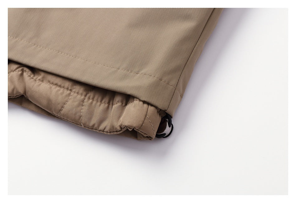 Close-up of a beige garment hem with gathered lining and a black cord toggle.