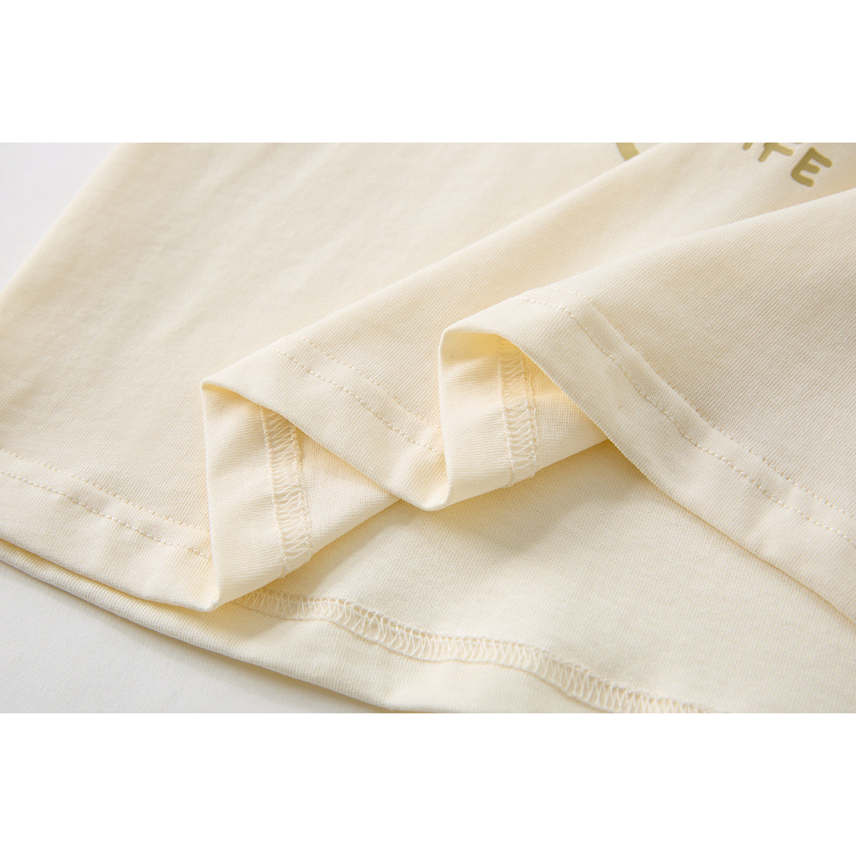 Close-up of the cream T-shirt's folded hem and visible stitching.
