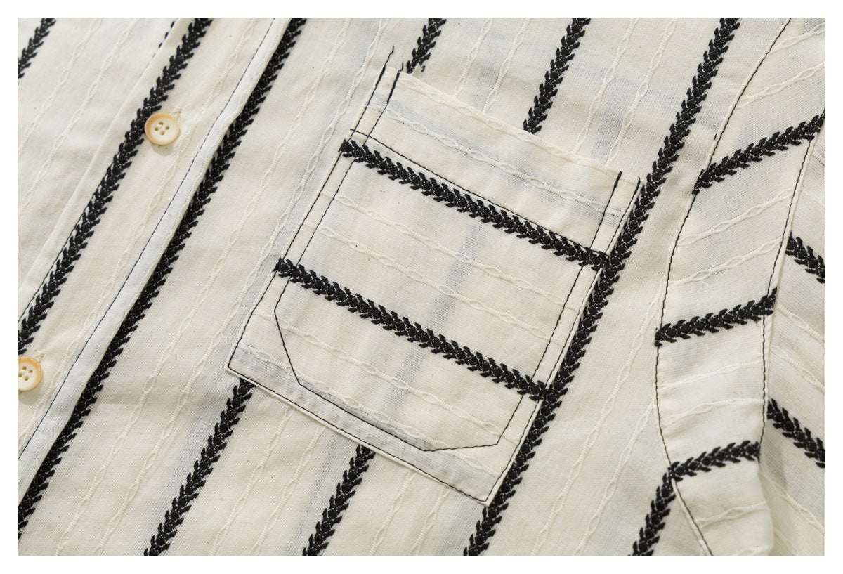 Close-up of an ivory shirt's chest pocket, with black braided stripes and raised stitched lines across the fabric.