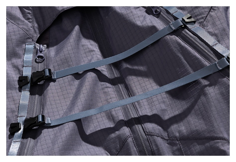 Close-up of a charcoal grid-pattern jacket with diagonal webbing straps, buckles and front zippers.