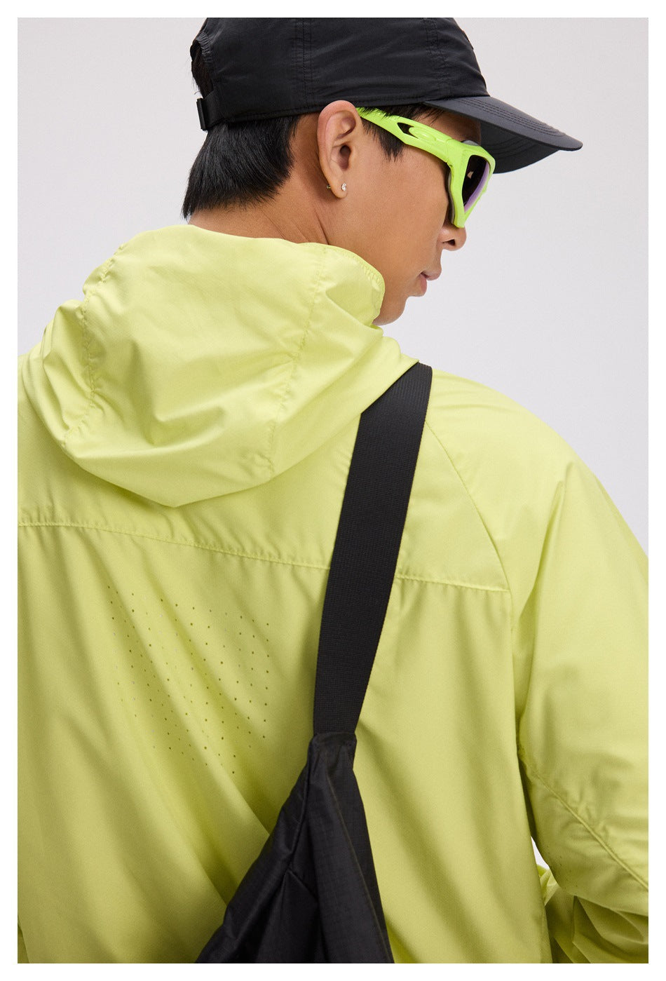 Close-up rear view of a lime hooded jacket showing the hood, back seams, and small perforated ventilation details.
