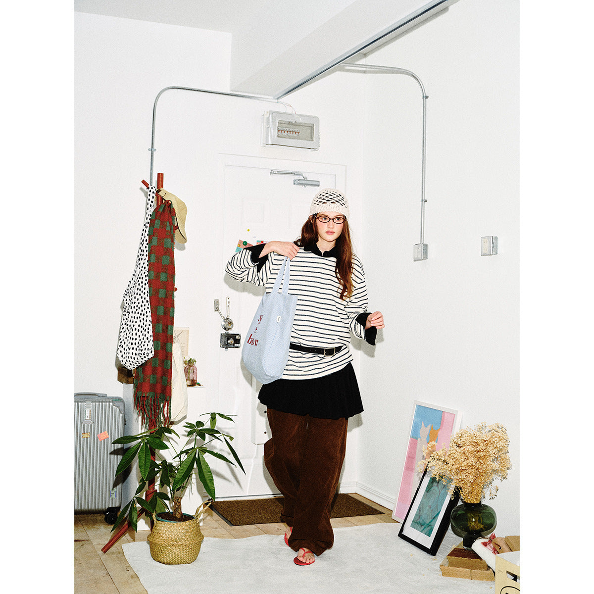Full-length model in an oversized cream-and-dark striped shirt with black cuffs, a black skirt, and loose brown trousers.
