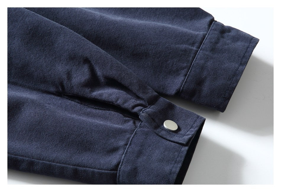 Close-up of a dark navy garment cuff with a silver snap tab and visible stitching.
