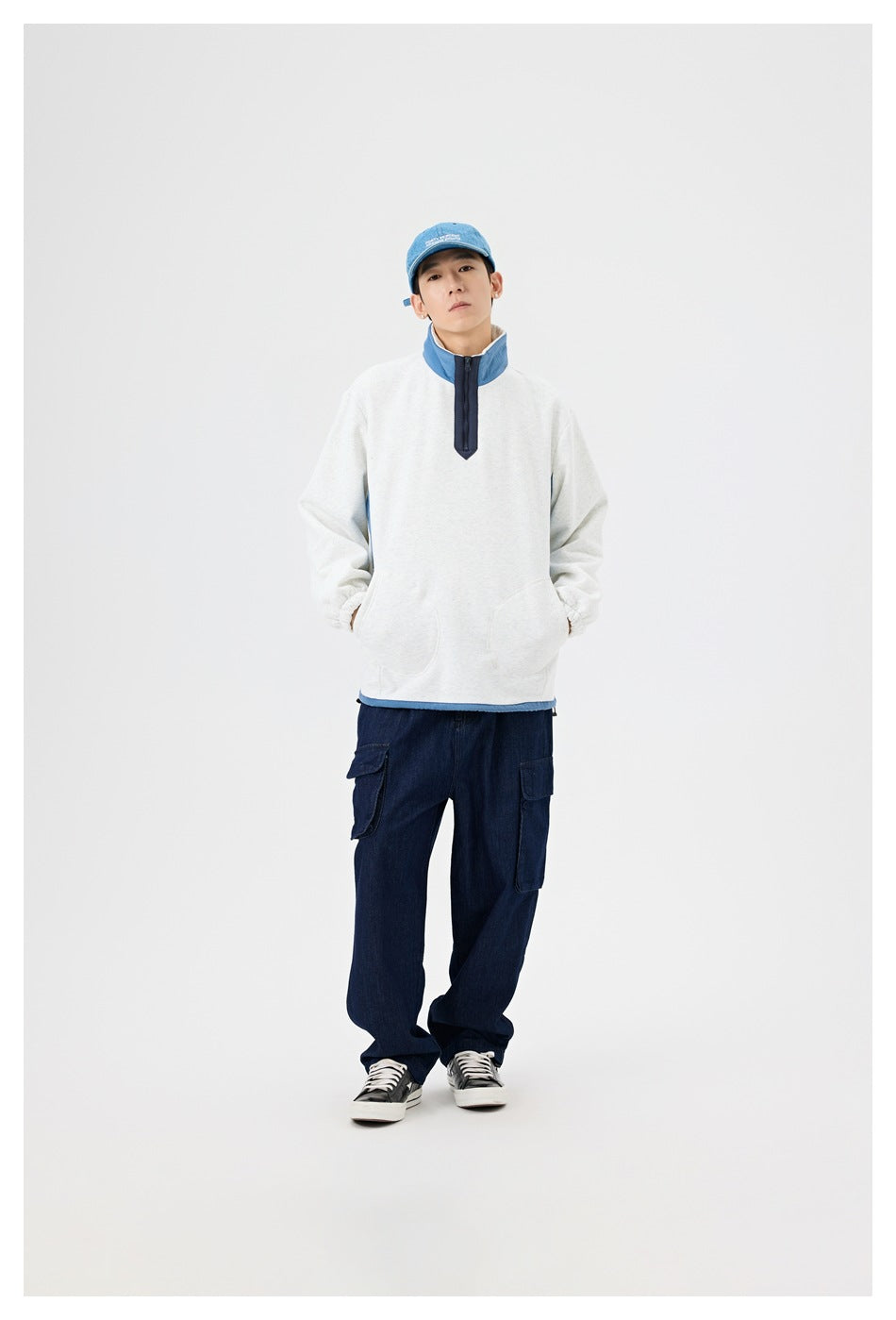 Model wearing a light gray quarter-zip pullover with a blue collar and navy cargo pants.