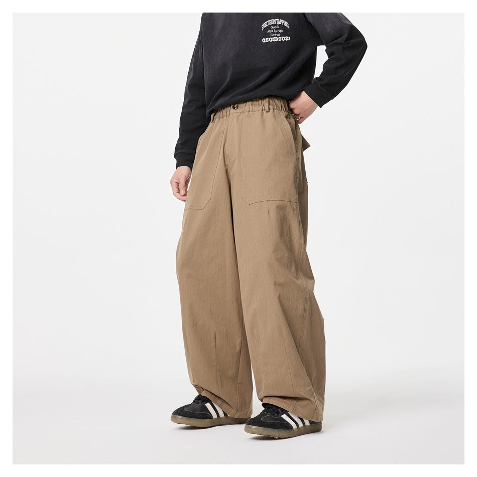Angled front view of a model wearing loose tan trousers with an elasticated waistband and front patch pockets.