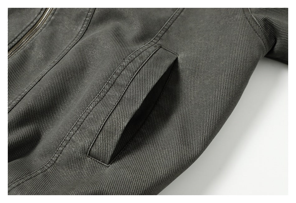 Close-up of a charcoal gray jacket's angled welt pocket, stitching, and partial zipper.