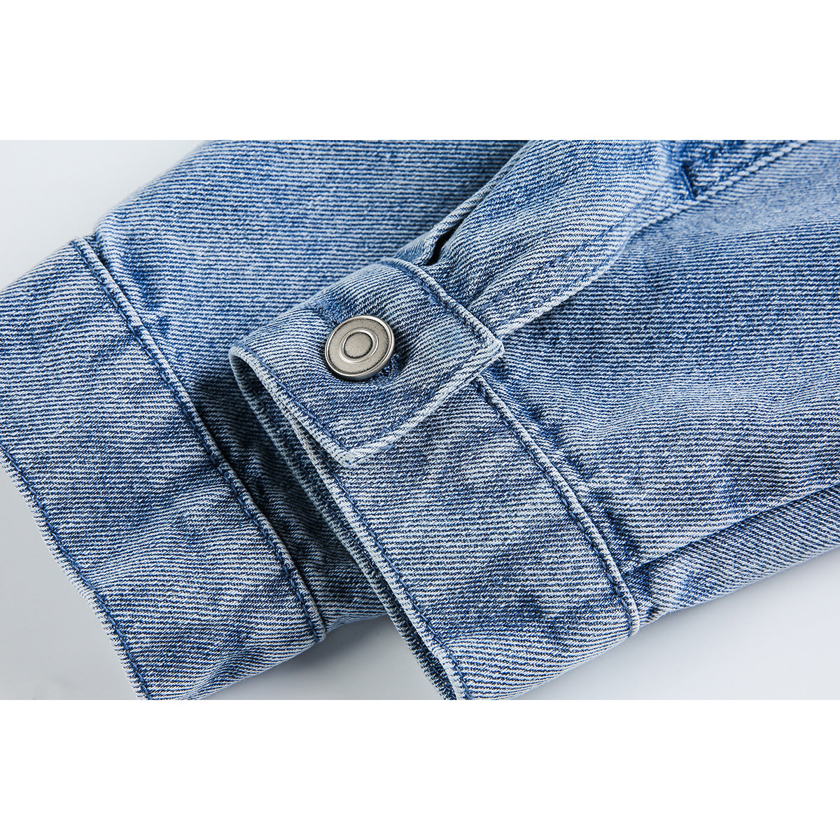 Close-up of a light blue denim jacket cuff with a round silver-tone button and stitched seams.