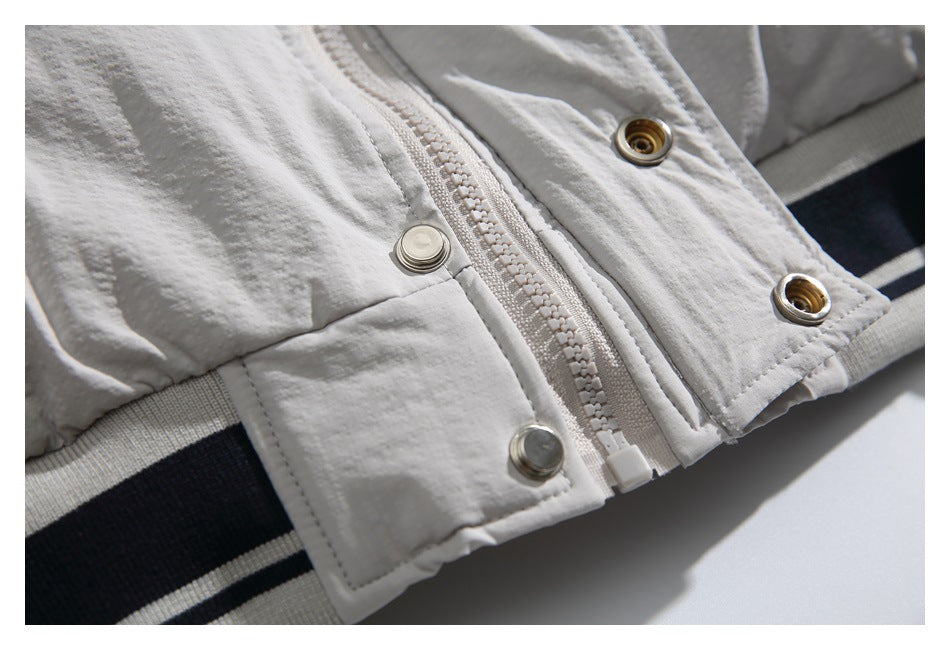 Close-up of a light gray jacket front with a zipper, metal snap fasteners, and a dark striped ribbed edge.