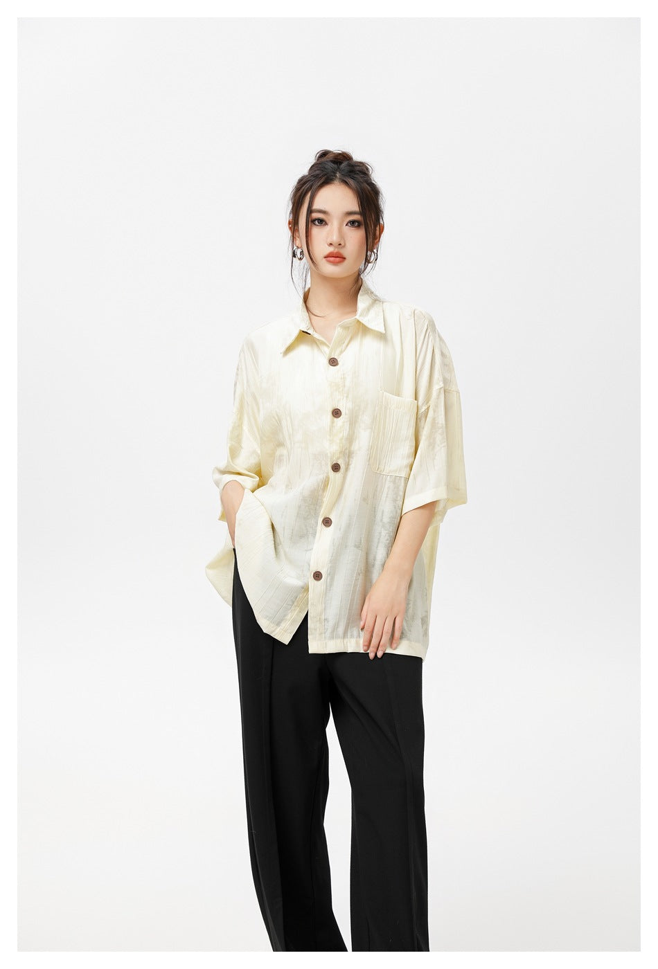 Model wearing an oversized ivory short-sleeve button-up shirt with a chest pocket and black trousers.