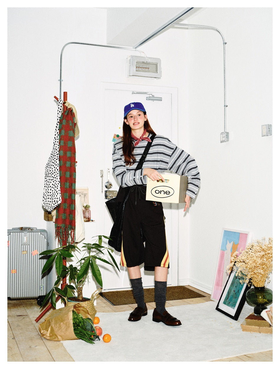 Front view of a model wearing a gray-and-black striped top and black shorts with red and yellow side stripes.
