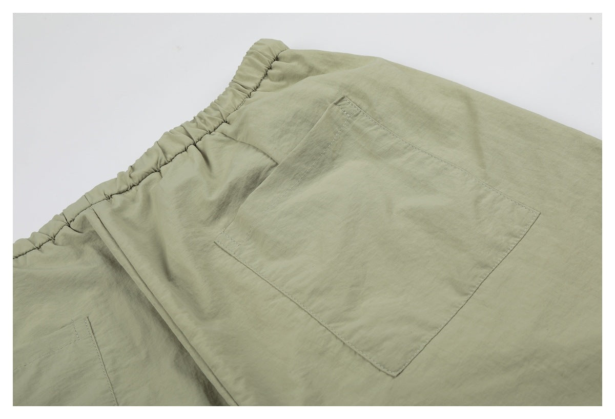 Close-up of sage-green shorts showing an elastic waistband and a large rectangular patch pocket.