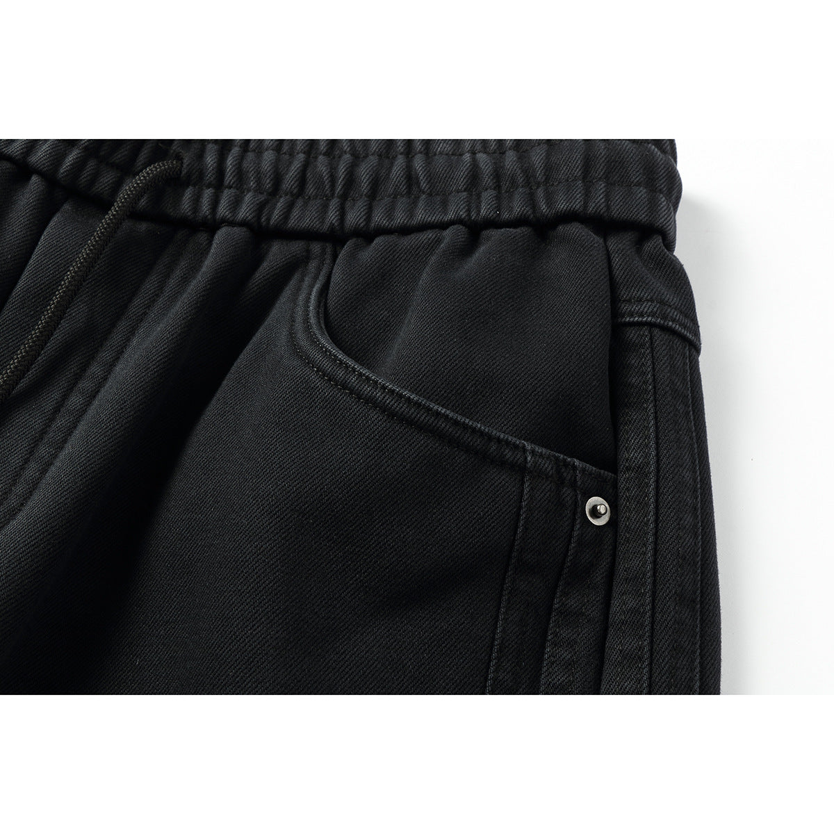 Close-up of a black pants pocket with stitched edging and a small metal rivet beside the elastic waistband.