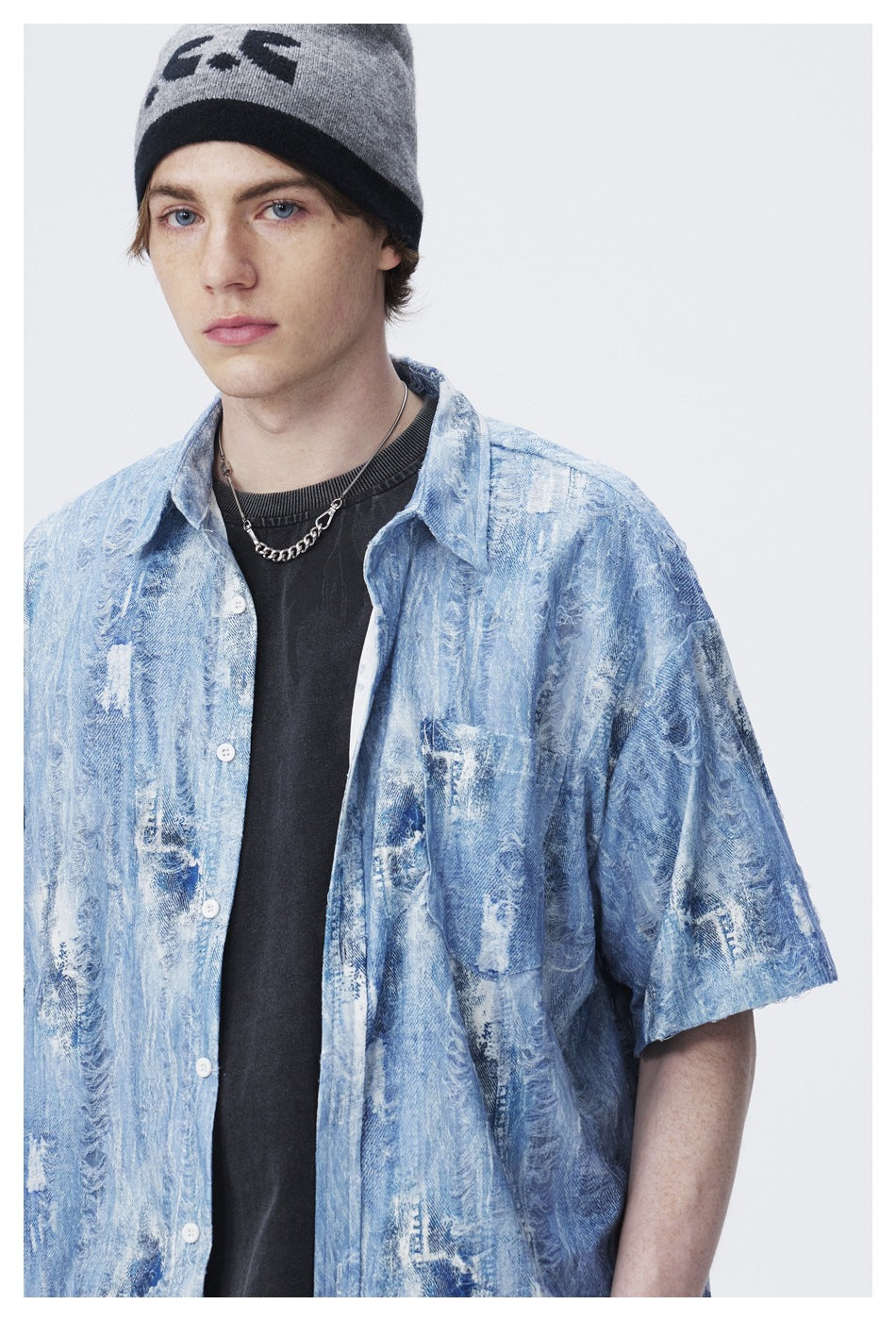 Close view of a model wearing a light blue distressed-pattern short-sleeve shirt over a black T-shirt.