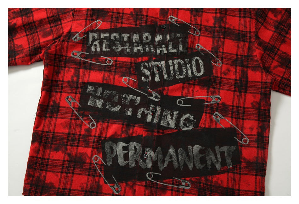 Close-up of distressed lettering and safety-pin graphics printed on the red-and-black plaid shirt.