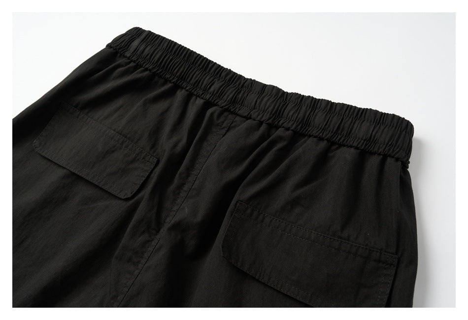Upper back view of black pants with a gathered elastic waistband and two flap pockets.