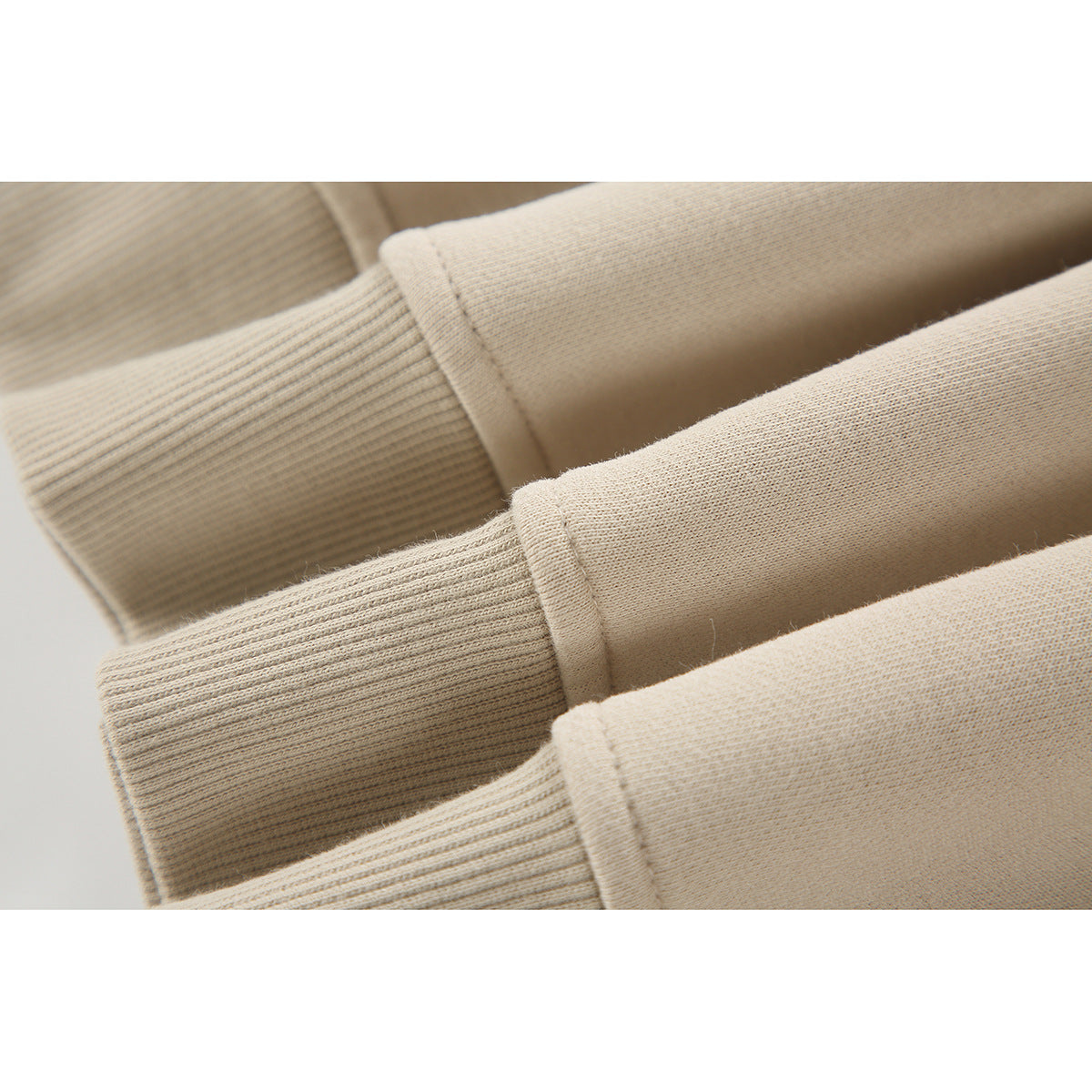 Close-up of several beige sweatshirt sleeves with ribbed cuffs and smooth fabric.