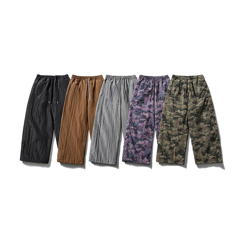 Five pairs of loose drawstring pants shown in black, brown, gray, purple camouflage, and green camouflage.