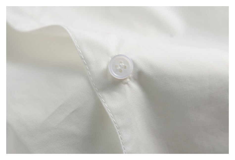 Macro view of a white four-hole button and stitching on white shirt fabric.