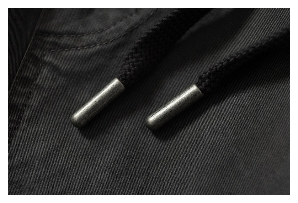 Close-up of black drawstrings with metal tips against charcoal pants fabric.