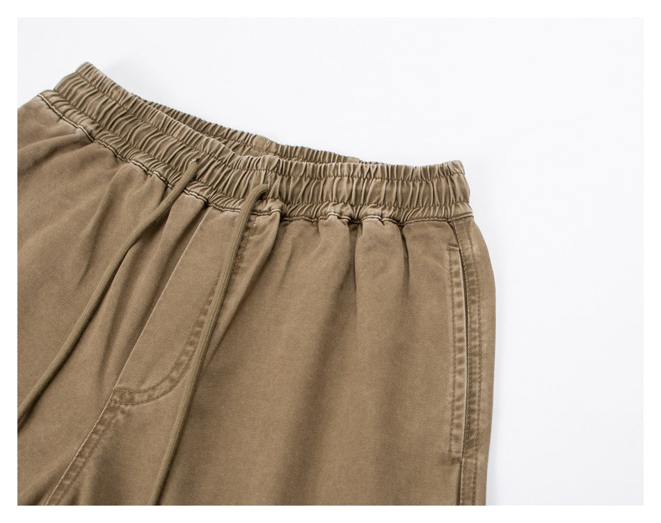 Close-up of tan pants showing the elastic waistband, drawstring, front pocket opening and side seam.