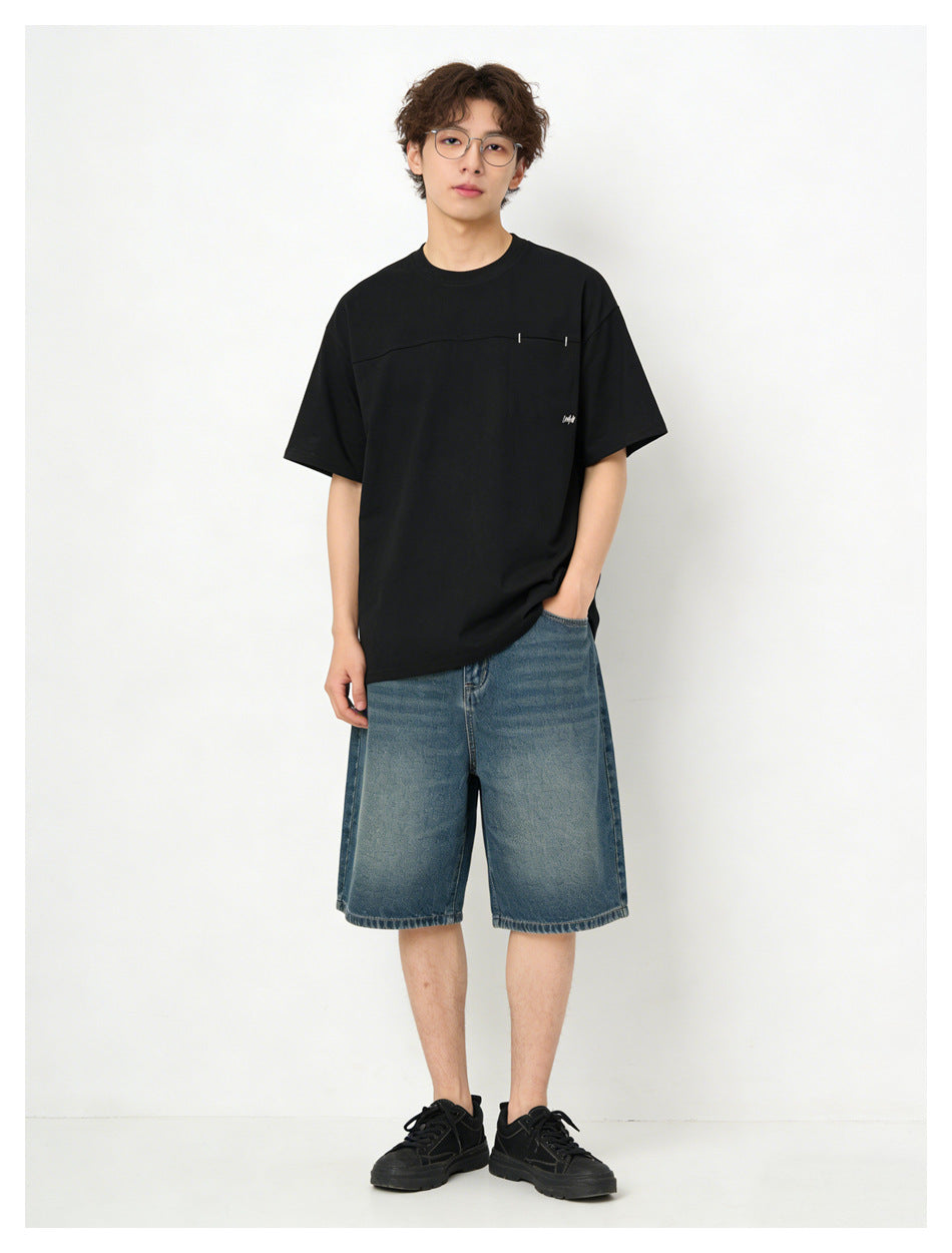Model wearing a black short-sleeve T-shirt with a horizontal chest seam and blue denim shorts, front view.