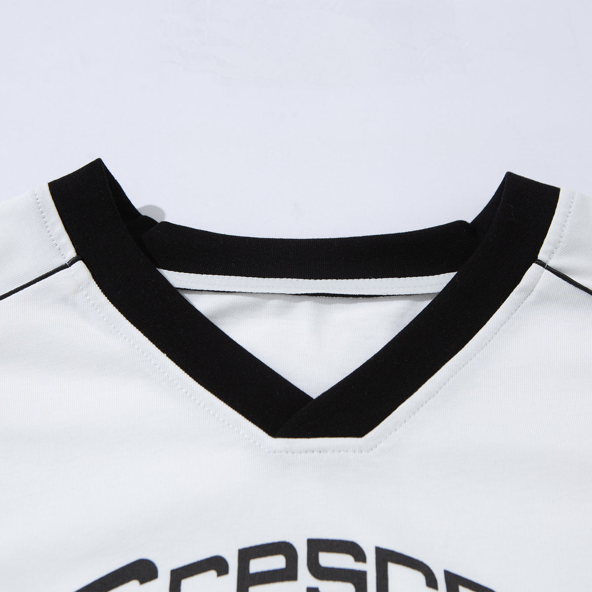 Close-up of a white T-shirt’s black V-neck trim and partial black chest graphic.