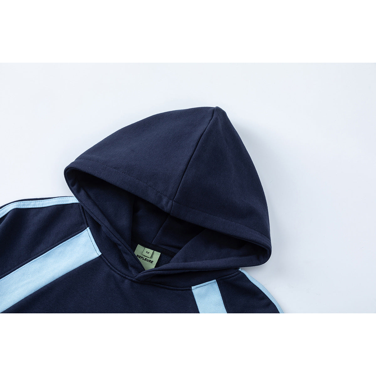 Close-up of a navy hoodie hood and shoulder with light blue panels and a small sewn neck label.