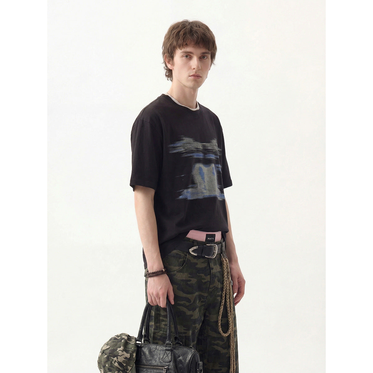 Model wearing a black short-sleeve T-shirt with an abstract blue-gray chest graphic and camouflage pants.
