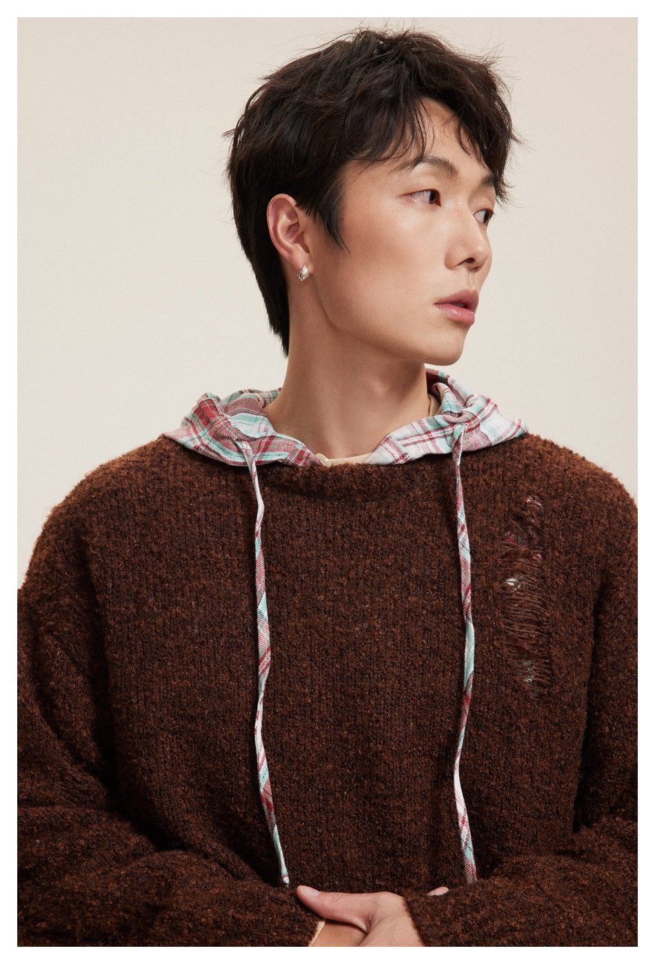 Close-up of a model wearing a dark brown textured sweater with a plaid hood and long drawstrings.