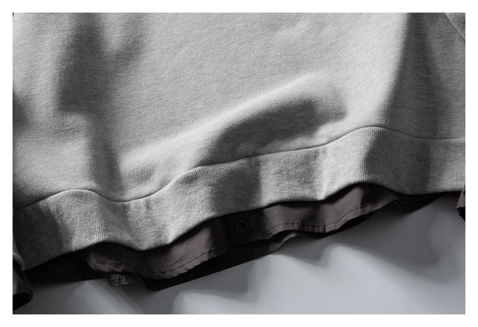 Close-up of a light gray sweatshirt hem with a dark shirt layer and button visible underneath.
