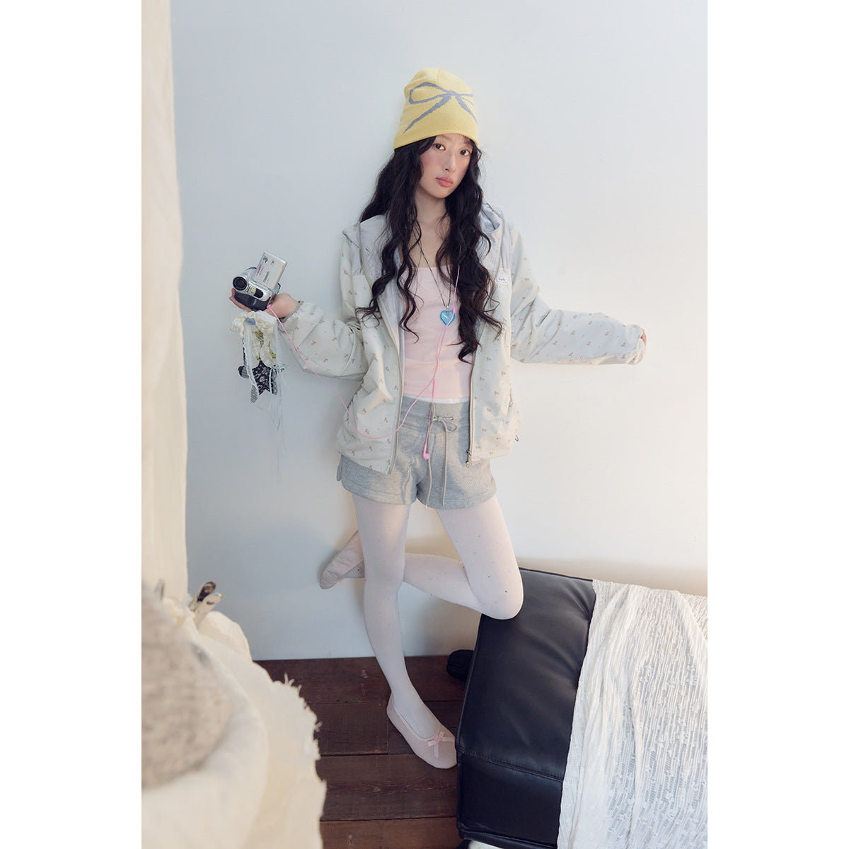 Model poses in an off-white printed hooded jacket and gray shorts, with dotted tights and a yellow beanie.