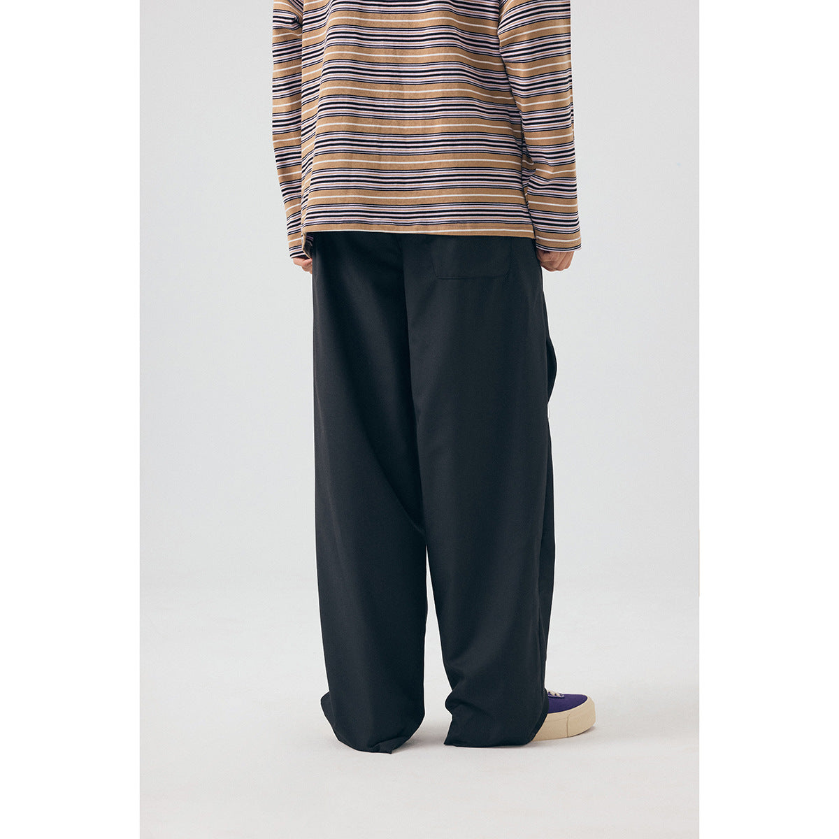 Back view of a model wearing wide-leg black trousers, showing a rear pocket and a tan striped shirt.
