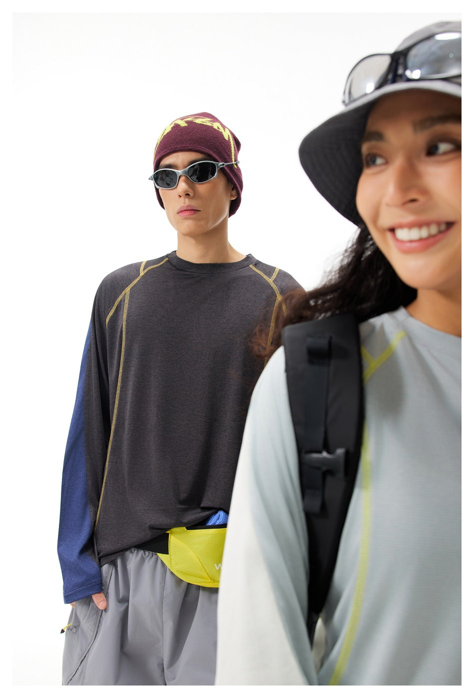 A model wears a charcoal long-sleeve top with blue sleeves and gray shorts; another model is cropped in the foreground.