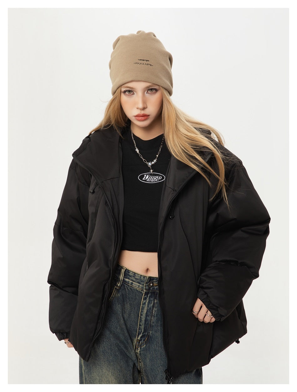 Close view of a model wearing an open black puffer jacket, beige beanie and black crop top.