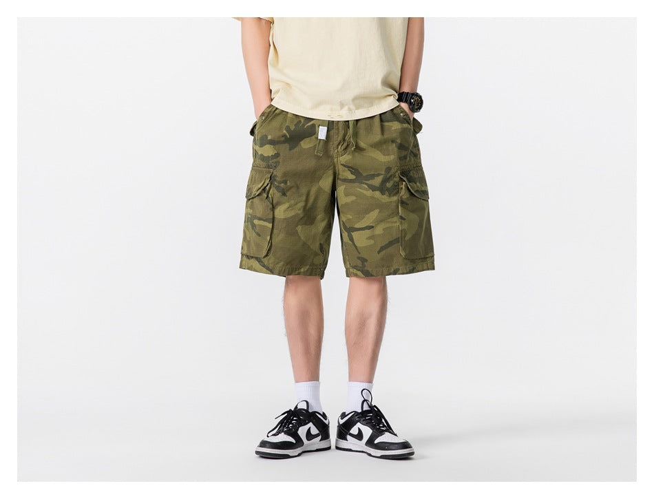 Model wearing olive camouflage cargo shorts with large side pockets, shown from the front.