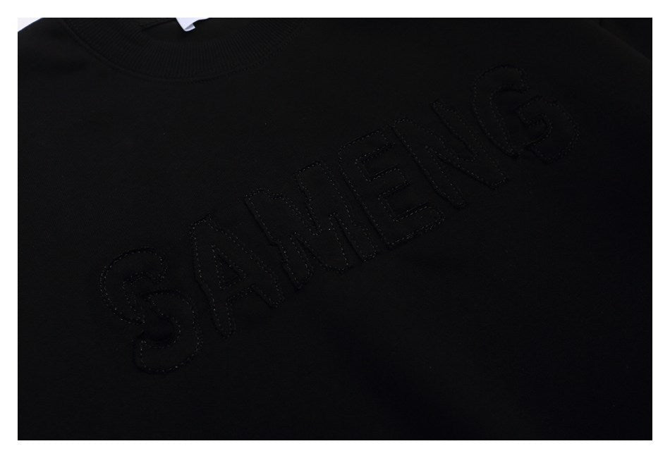 Close-up of raised black lettering across the chest of a black sweatshirt.