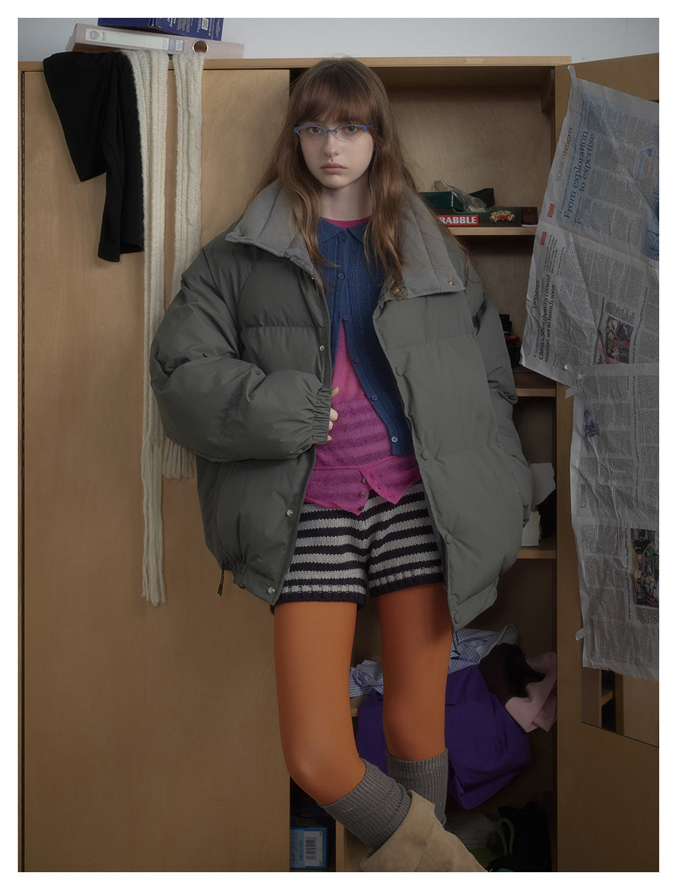 Closer view of a model in an open charcoal-gray puffer jacket with a wide collar, snap front, and roomy sleeves.