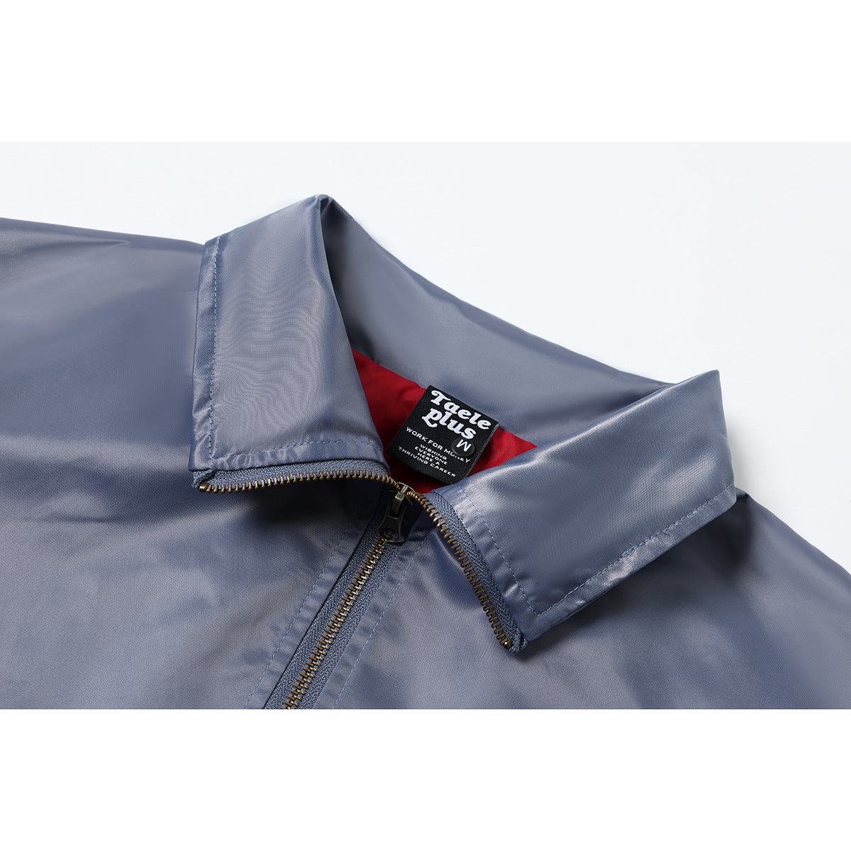 Close-up of a slate blue jacket’s pointed collar, brass-tone zipper and inner neck label.